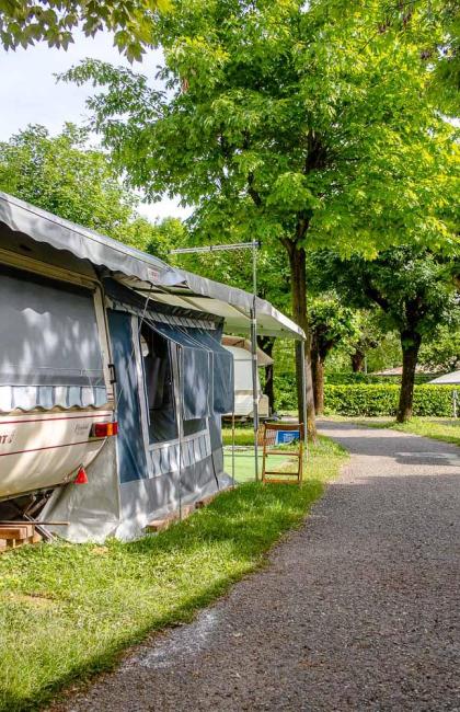 Campground with caravan, tree-lined path, parked cars, and fire extinguisher sign.