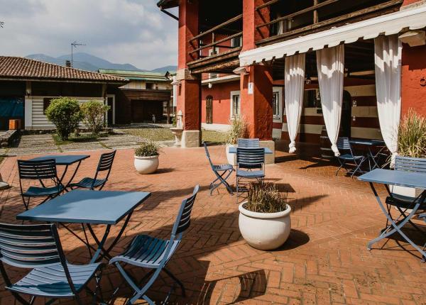 Terrazza con tavoli e sedie blu, edificio rosso e montagne sullo sfondo.