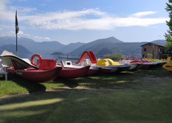 Pedalò colorati allineati sulla riva di un lago montano.